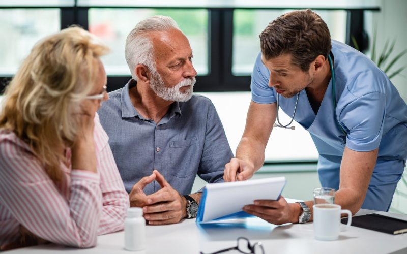 Serious doctor discussing with senior couple about their medical documents during appointment at clinic.